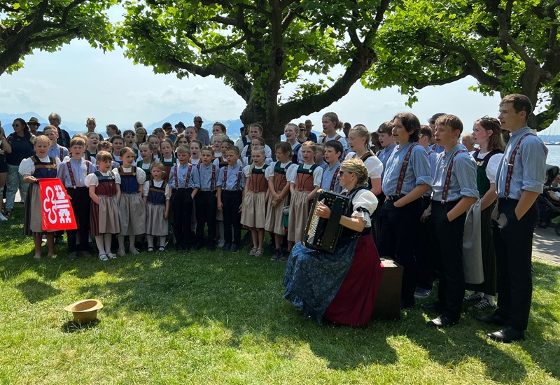 Kinderjodlercheerli singend mit Akkordeon 
				im Gras unter den Bäumen mit liegendem Hut